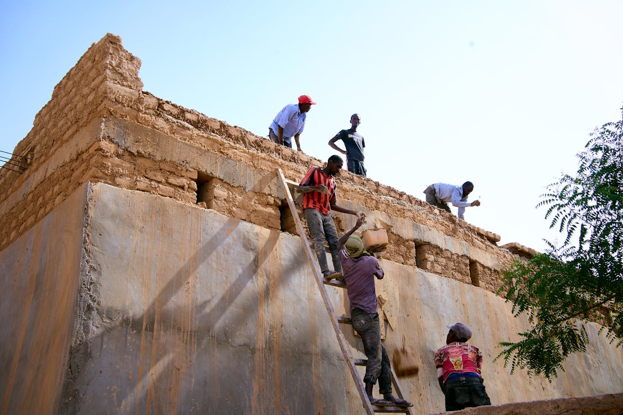 Workers constructing a traditional mud brick building under bright daylight.