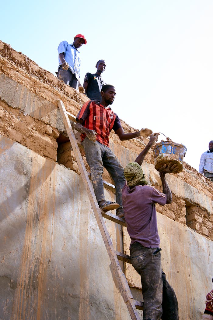 Workers actively building a mud brick structure using ladders and teamwork.