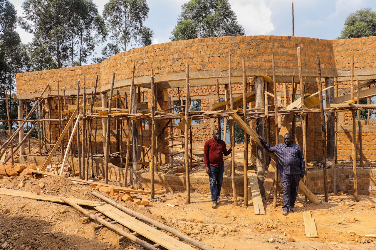 Two men inspect the wooden scaffolding of a brick building construction site outdoors.